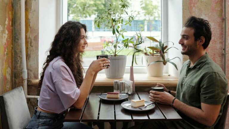 A smiling couple enjoys coffee and cake at a cafe table.
