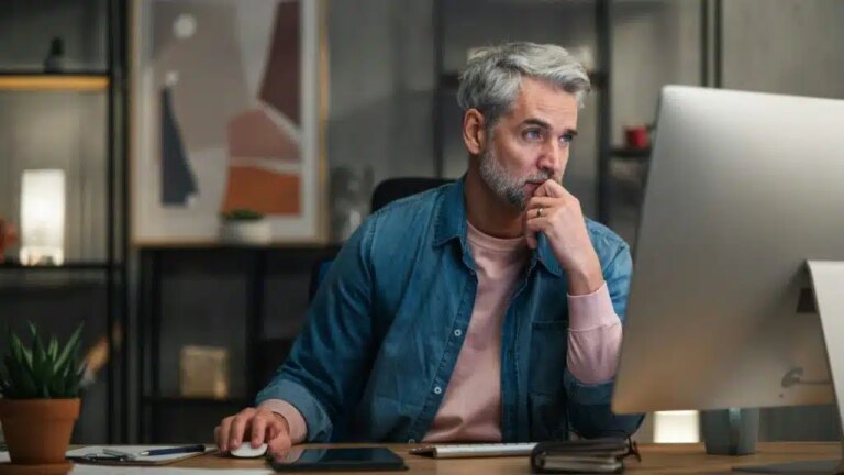 A focused man with gray hair and a beard uses a computer at a desk.