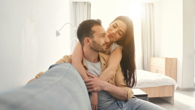 A happy couple embraces on a couch, bathed in warm sunlight.