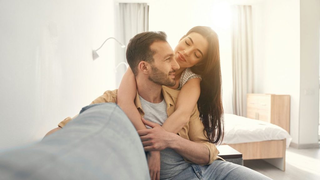 A happy couple embraces on a couch, bathed in warm sunlight.