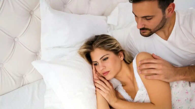 A man in a white shirt comforts a sad woman lying in bed.