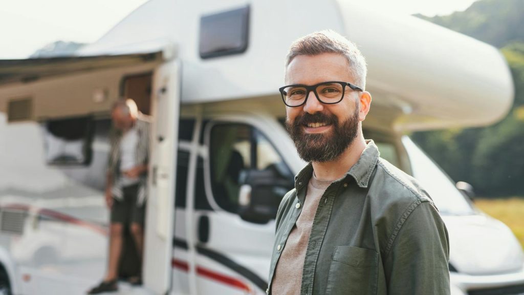A smiling bearded man with glasses in front of an RV.