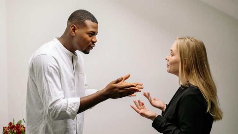 A man and woman face each other, gesturing with their hands as if in discussion.