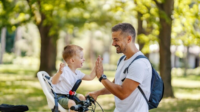 A man and a kid sharing a high five during a bike ride in a sunny park.