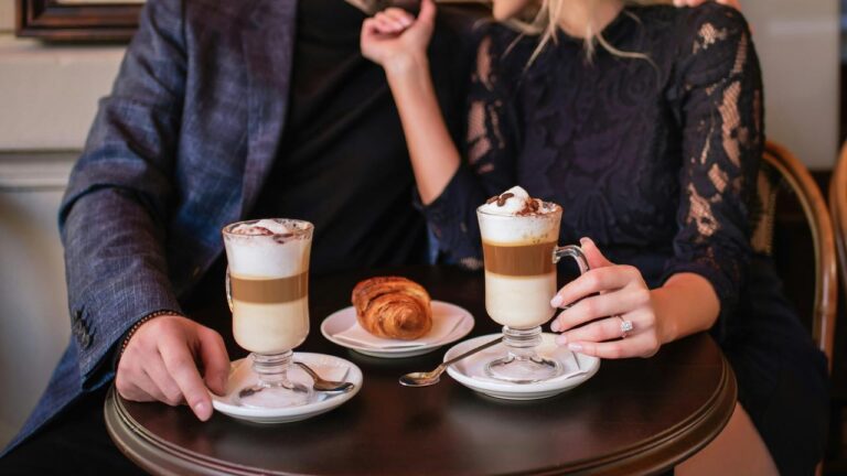 A couple enjoying lattes and a croissant at a café table.