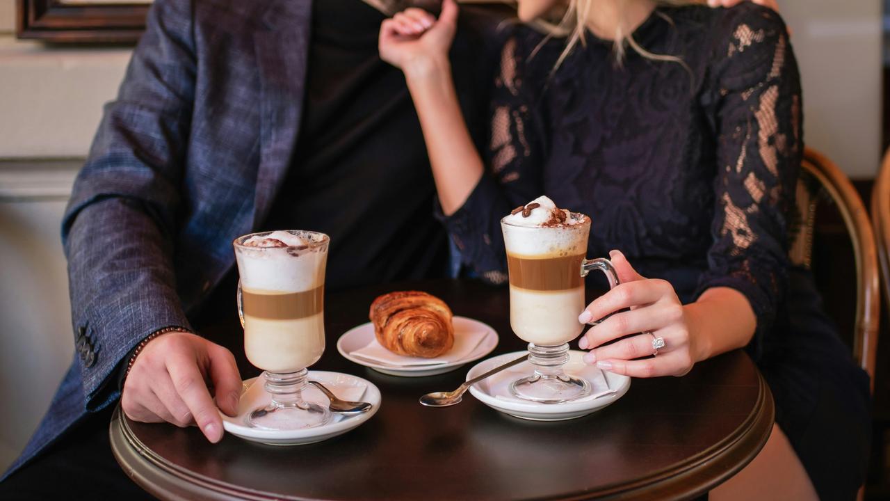 A couple enjoying lattes and a croissant at a café table.