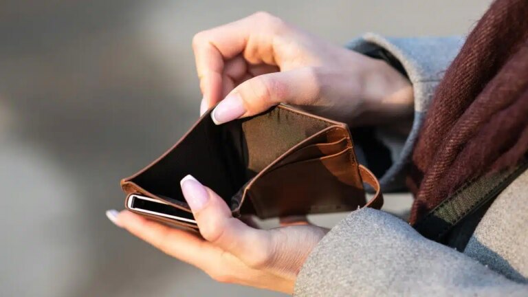 An empty brown wallet held open by a person with manicured nails.