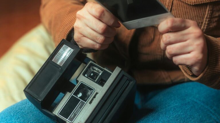 A person holding a Polaroid photo and instant camera.