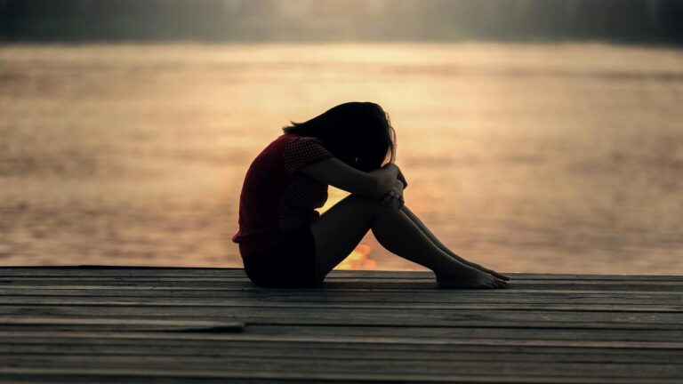 A woman looking sad by a body of water.