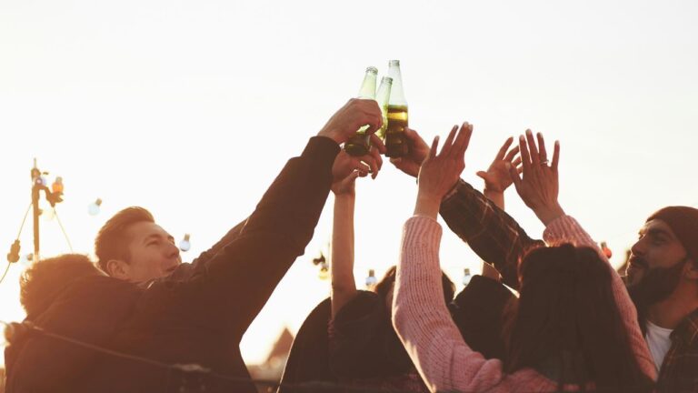 A group of friends raising beer bottles in a celebratory toast at sunset.