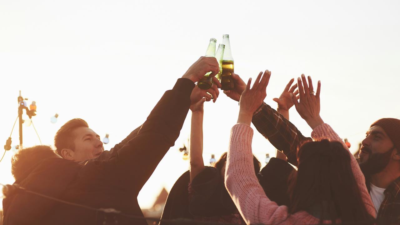 A group of friends raising beer bottles in a celebratory toast at sunset.